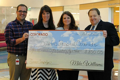 4 people smiling and holding a check for $8,850.05 that is being donated to the Children's Hospital of Colorado.